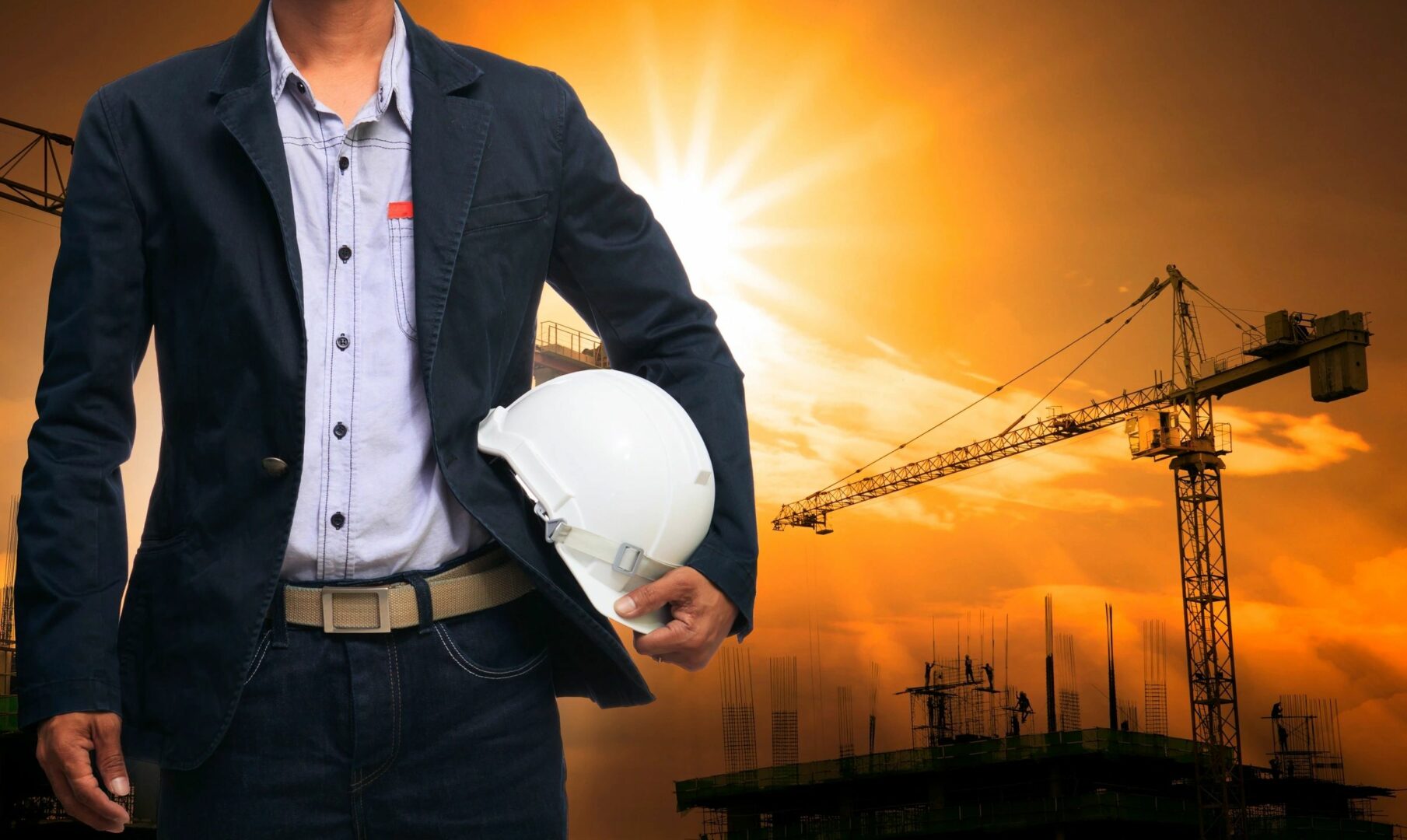 A man holding a white hard hat in front of an orange sky.